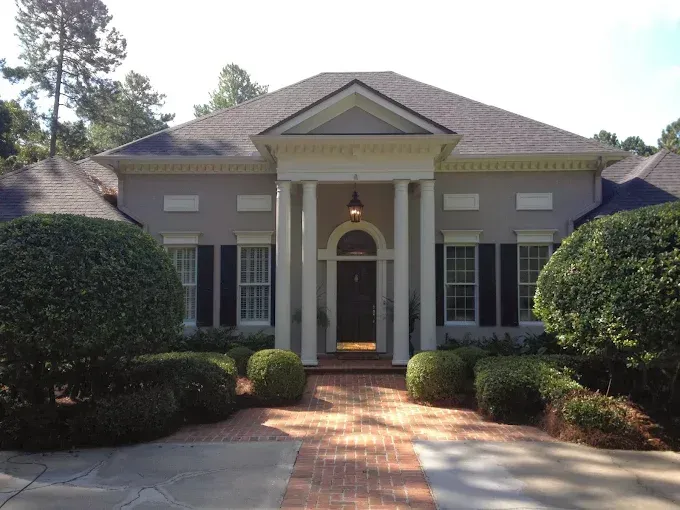 Gray house with white columns, black shutters, and a brick path leading to the front door.