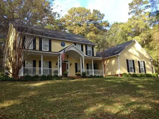 Yellow two-story house with white porch, black shutters, and an American flag.