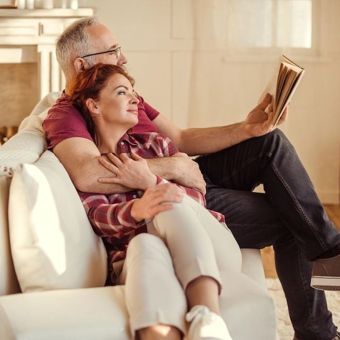 A man and a woman are sitting on a couch reading a book.