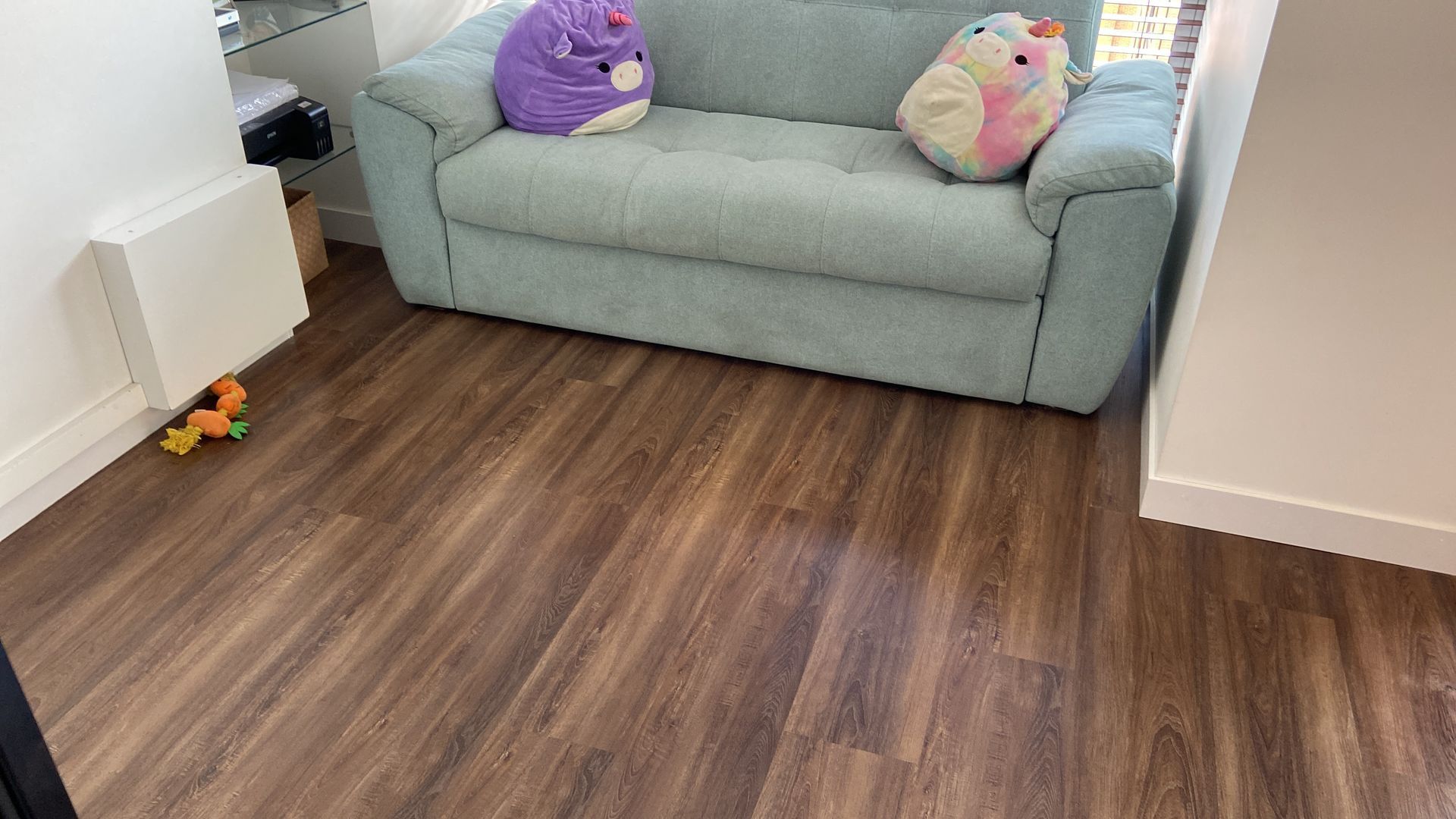 Un pequeño espacio de estar con pisos de apariencia madera, un sofá azul y juguetes de peluche coloridos.
