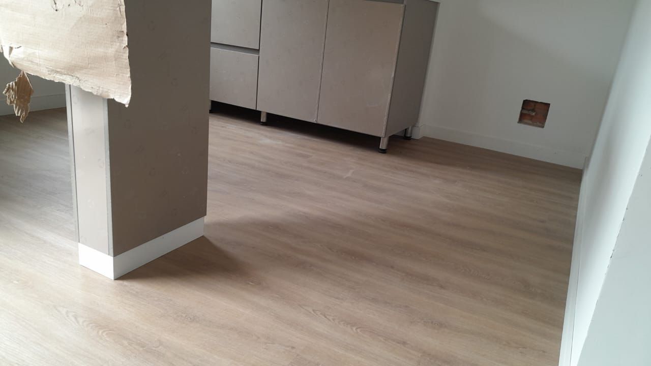 Habitación con suelo imitación madera, armarios en tonos neutros y una columna beige. Hay un agujero en la pared.