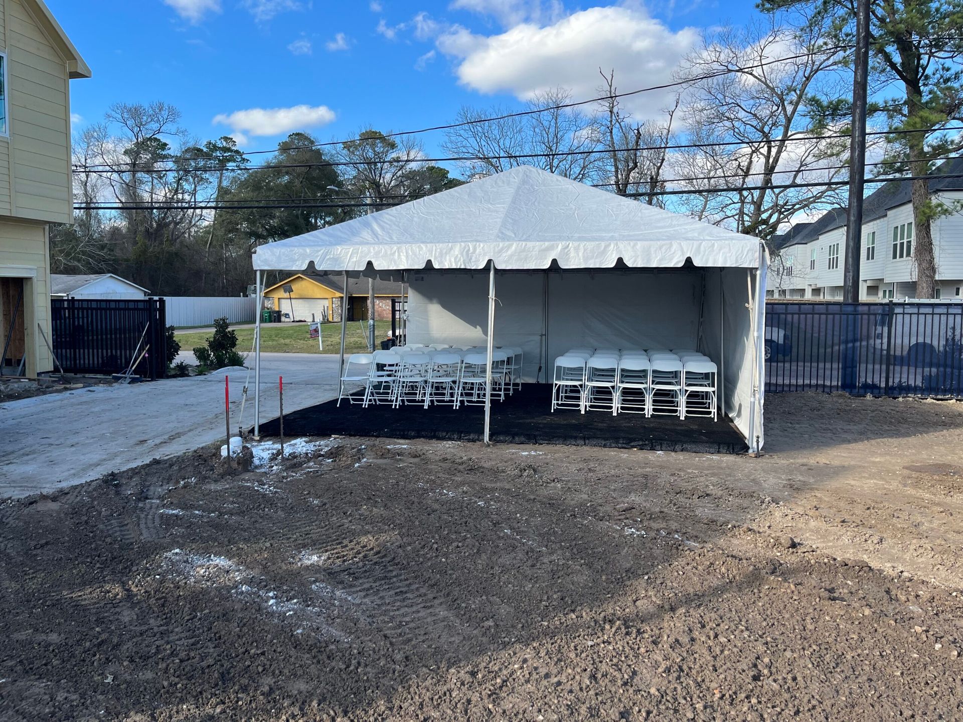 White tent set up outdoors, with chairs inside on black ground.
