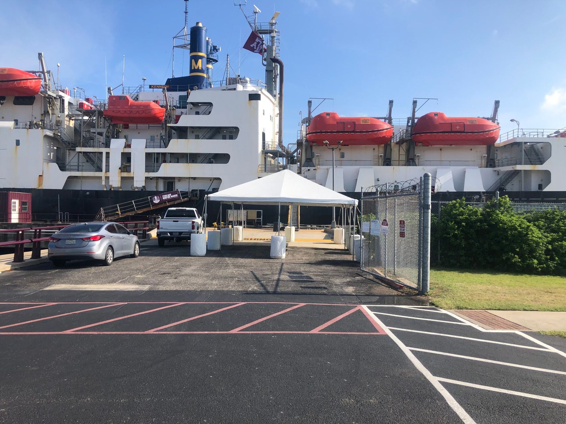 A tent entrance beside a large ship docked at a pier. Vehicles parked nearby.