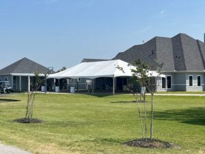 A large white tent set up on a green lawn in front of a gray house.