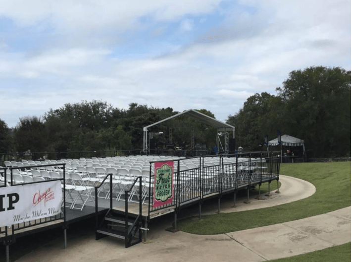 Outdoor event space with rows of chairs facing a stage set up under a white tent.