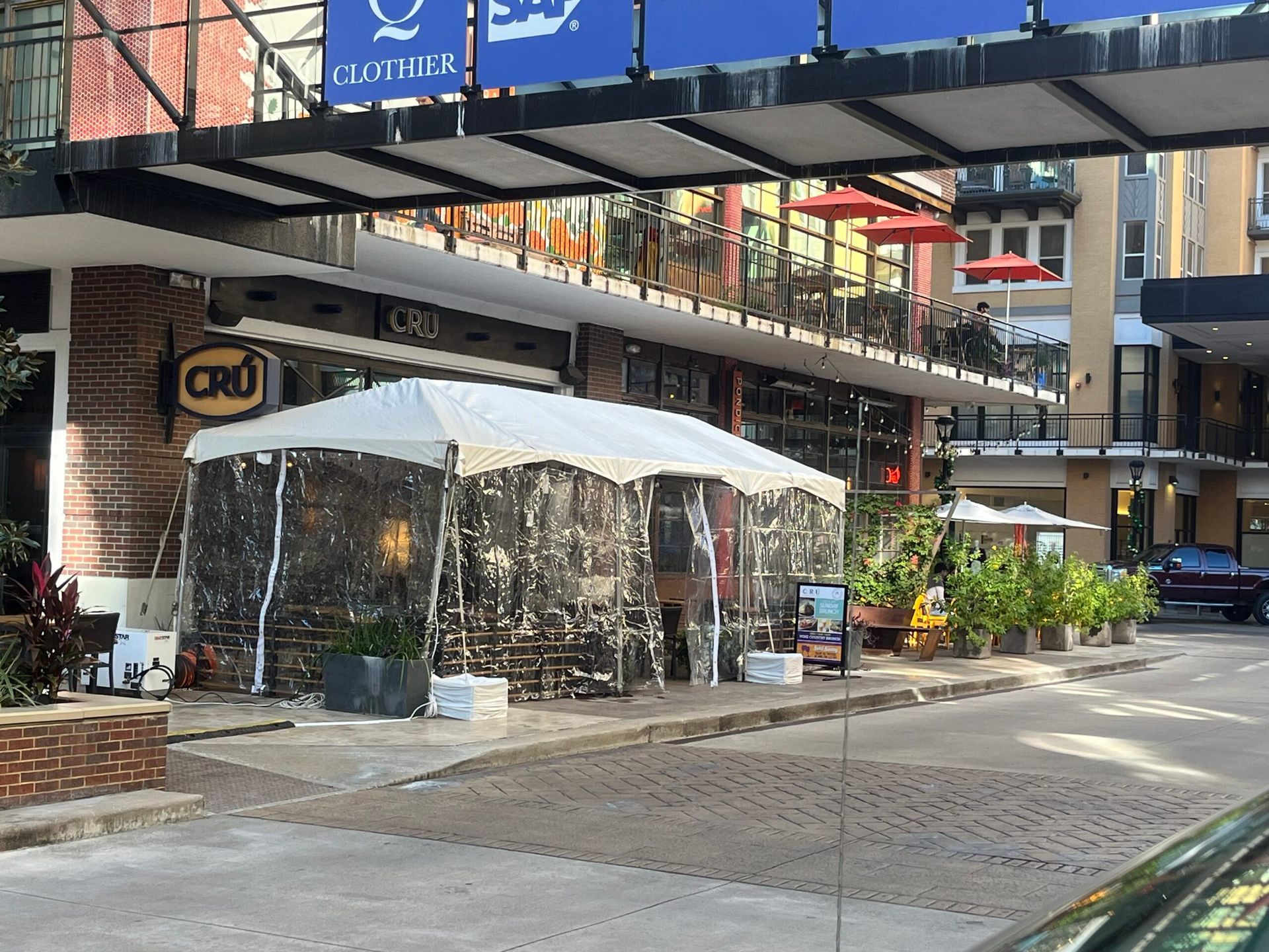 Outdoor dining area under awning, covered tent, brick building, plants.