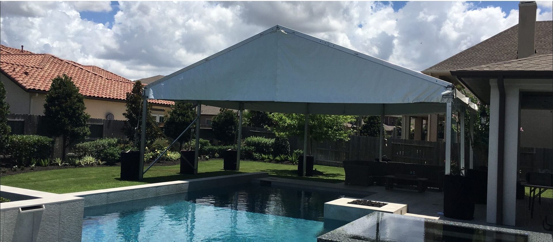 A white canopy covers a pool, with a house visible in the background under a blue sky.