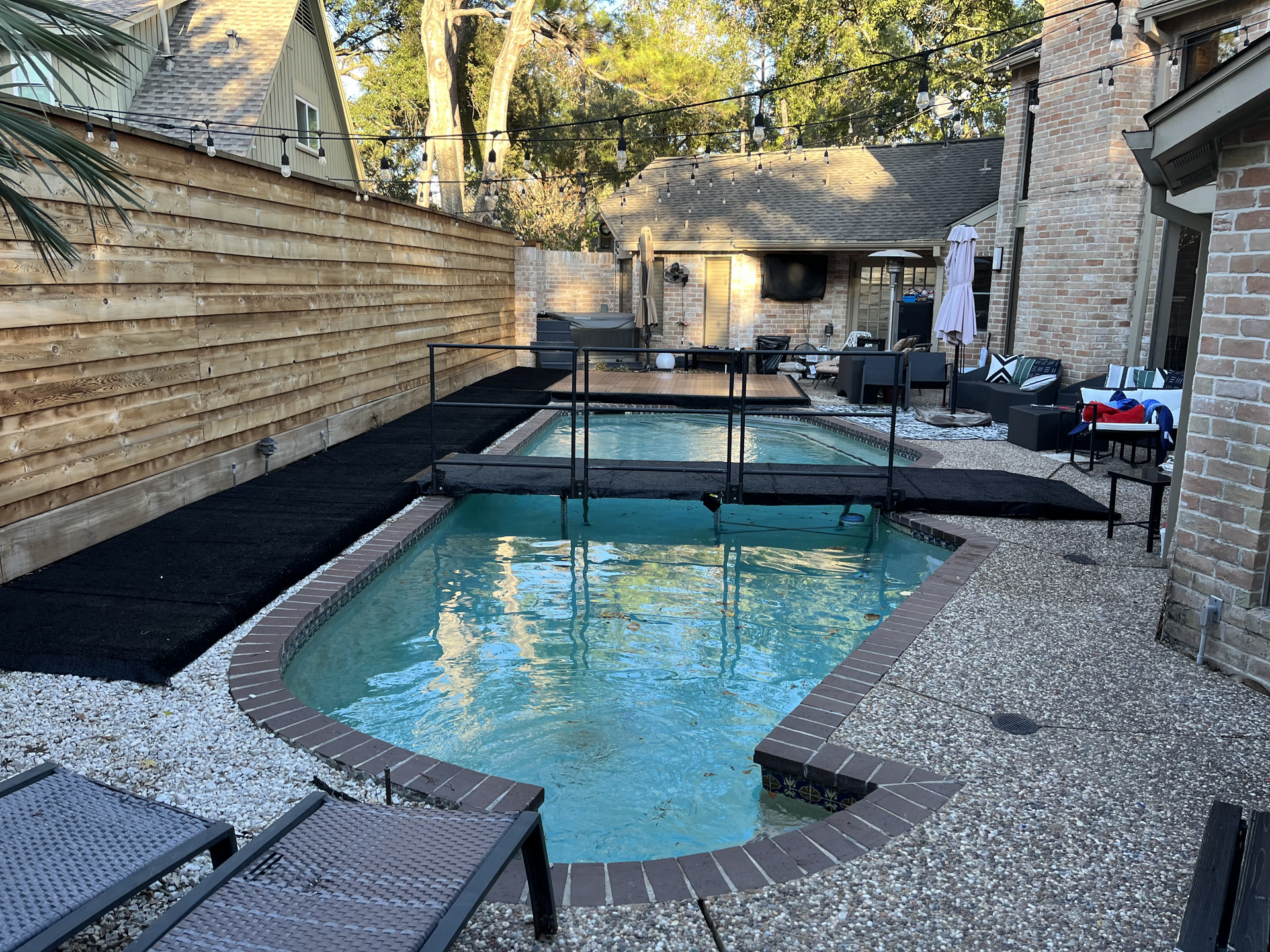 Backyard pool with stone patio, lounge chairs, and wooden privacy fence.
