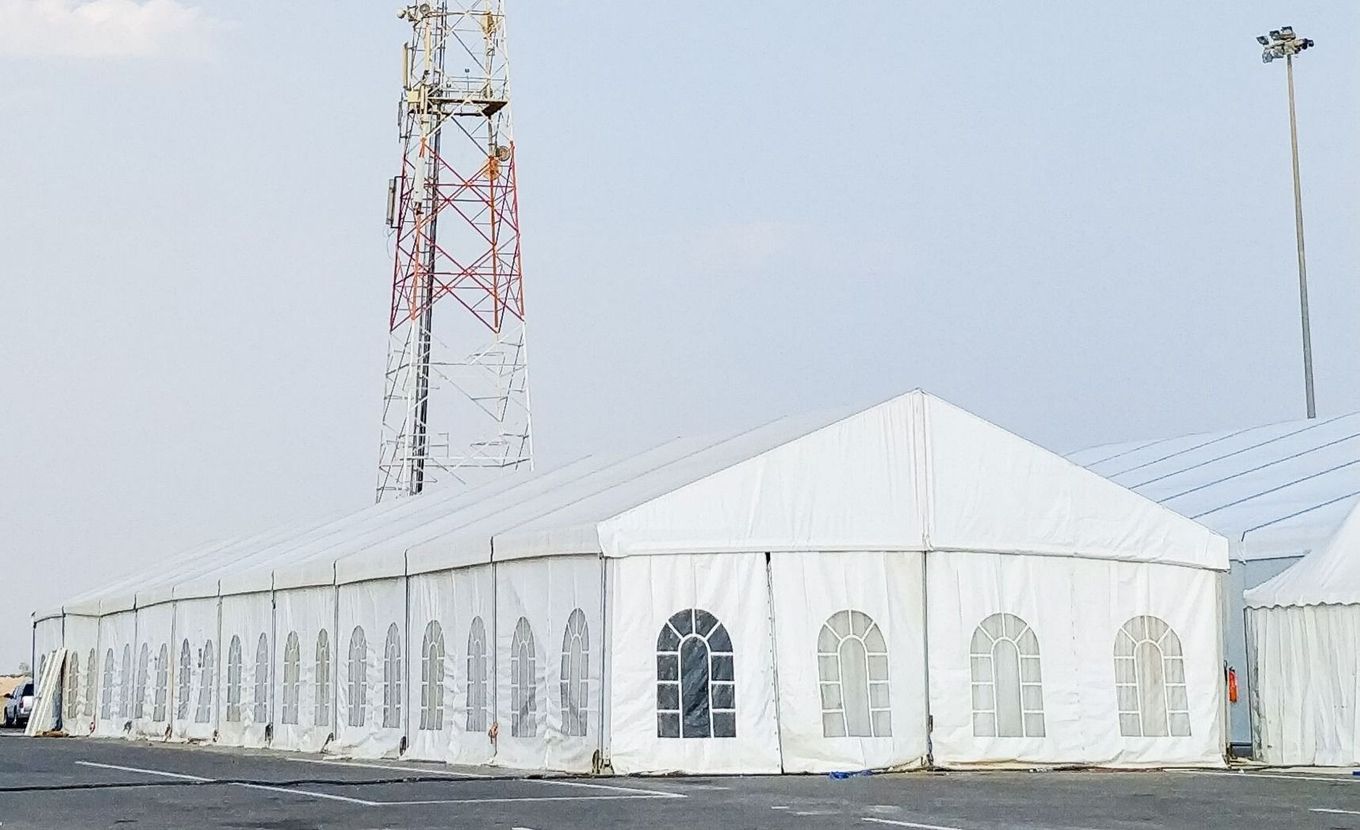 White tents in an outdoor setting, near a communication tower.