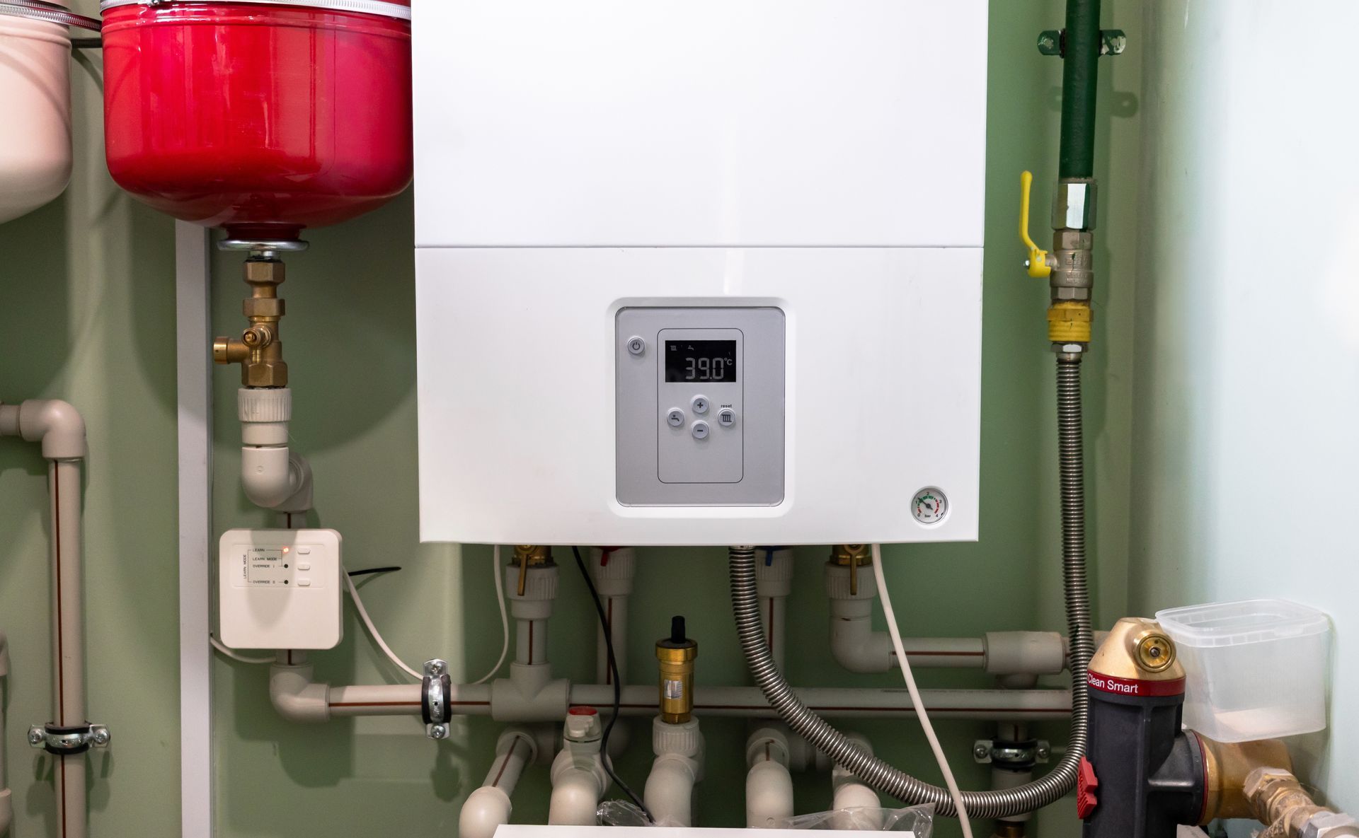 Wall-mounted boiler with pipes, gauges, and a red expansion tank in a utility room.