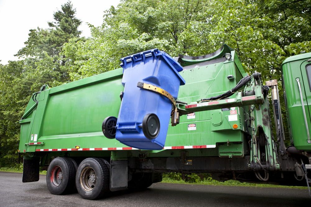 A Green Garbage Truck With A Blue Trash Can Attached To It — Eco Skips In Bowen, QLD