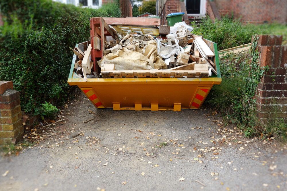 A yellow dumpster filled with wood is parked in a driveway — Eco Skips In Midge Point, QLD