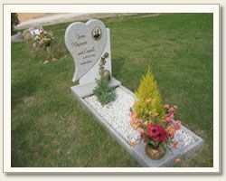 Una tomba con una lapide a forma di cuore e fiori sopra in un cimitero.