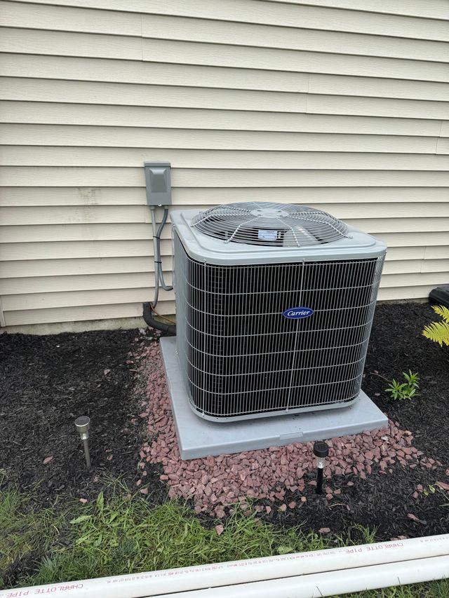 Outdoor air conditioner unit beside a beige house wall on a concrete pad with mulch around it