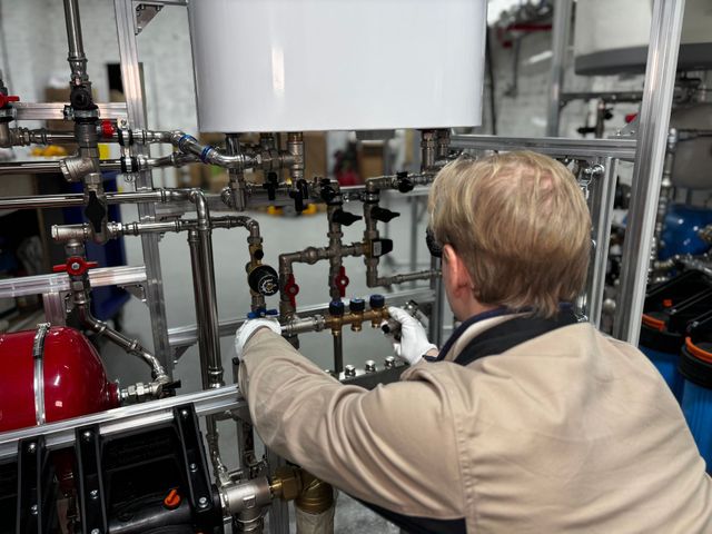 Technician in beige jacket adjusting pipes and valves in an industrial lab