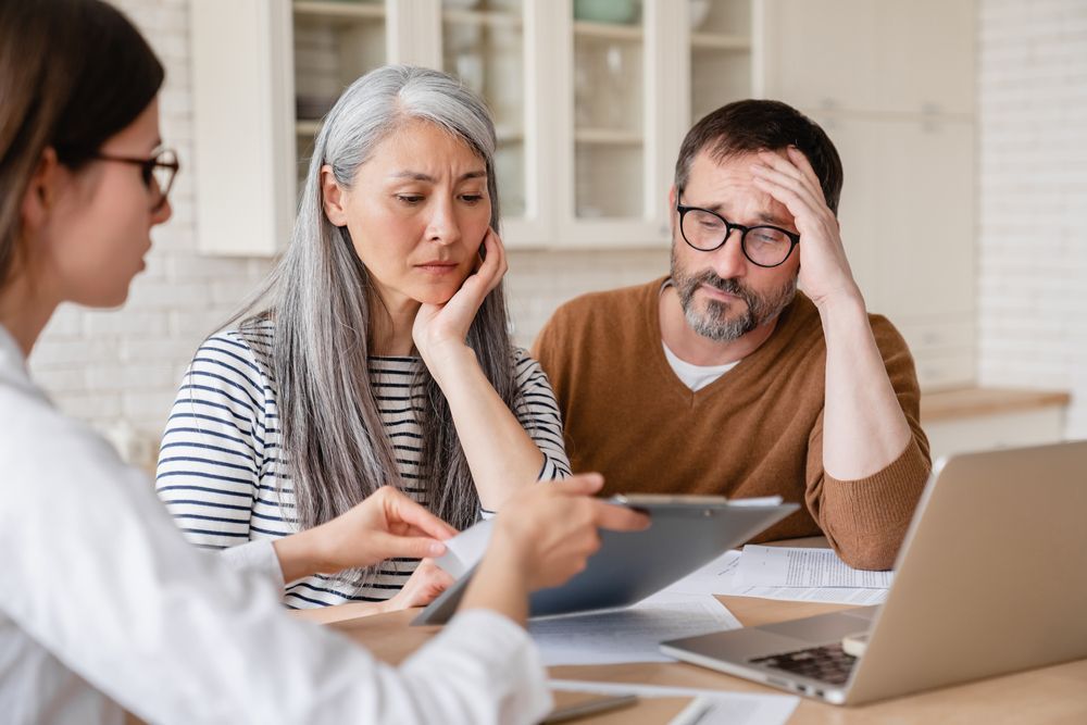A woman shows a document to a concerned couple at a kitchen table. 