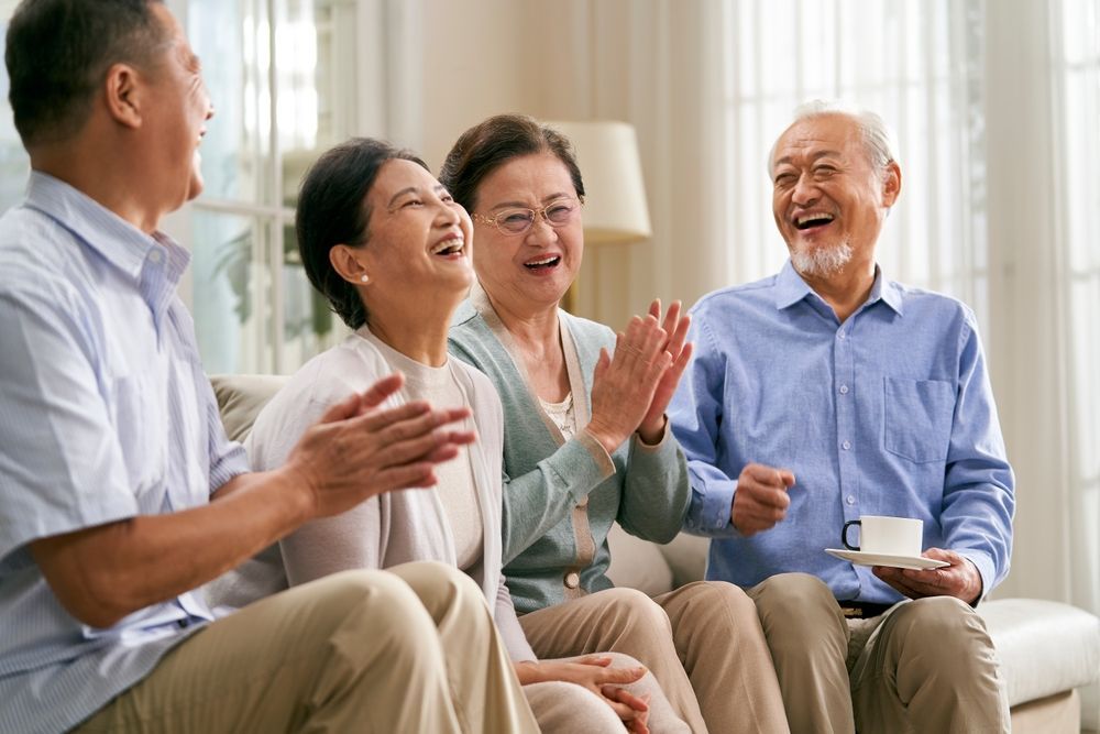Four people laughing and clapping, seated on a couch indoors.
