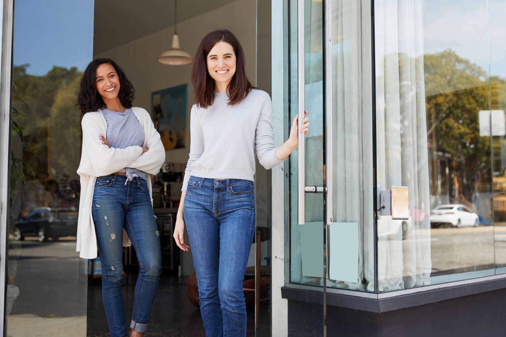 Two women smiling at doorway of a business. 