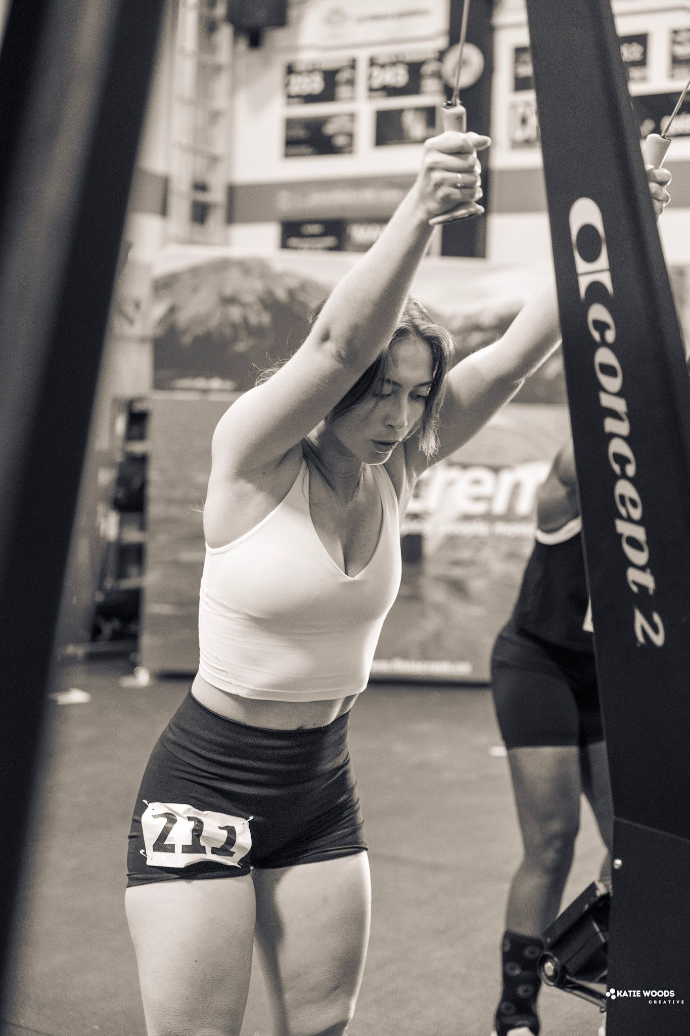 Femme en haut blanc et short noir s'étirant sur un rameur Concept2, les bras au-dessus de la tête.