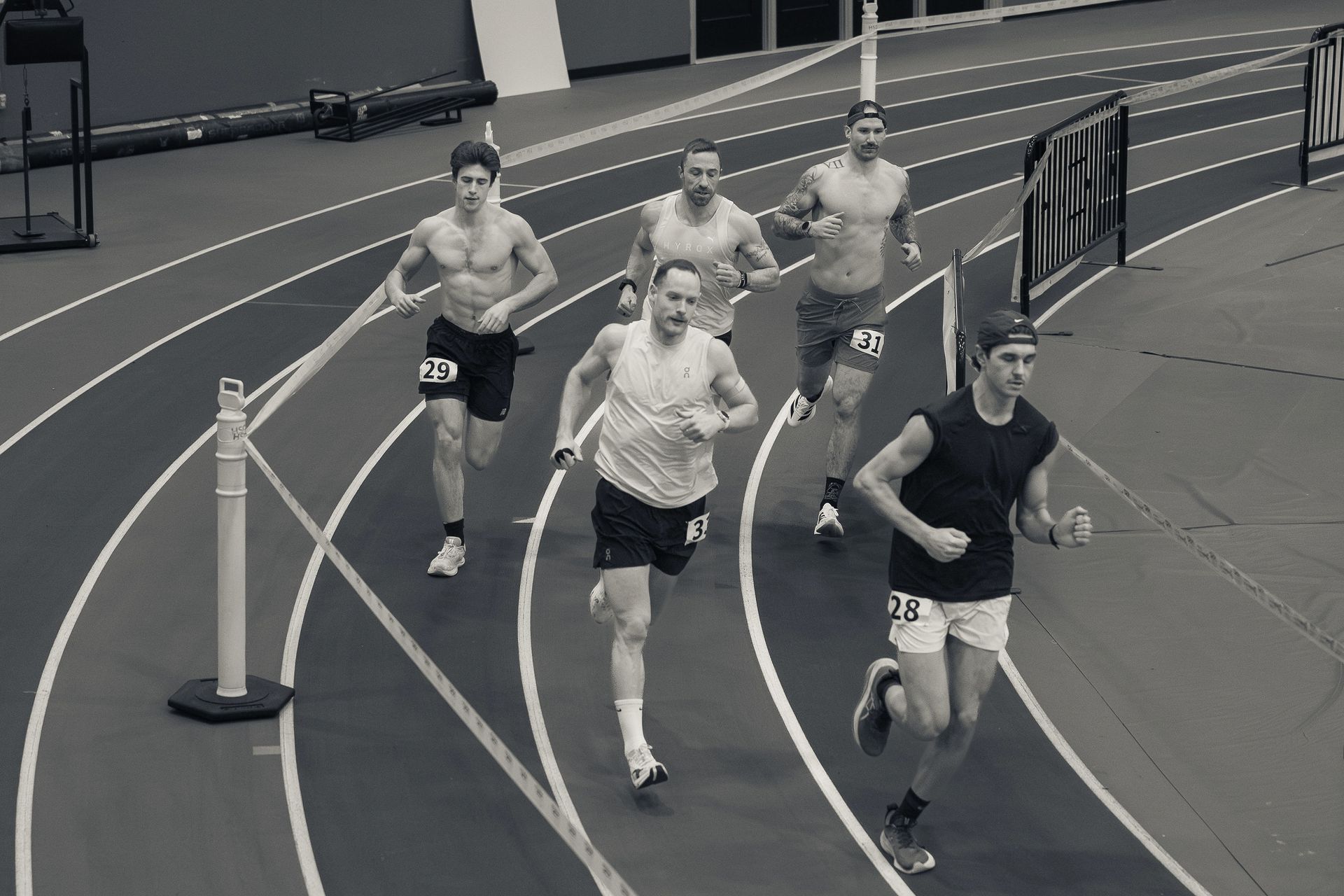Des coureurs s'affrontent sur une piste intérieure ; des hommes en noir et blanc sprintent vers la ligne d'arrivée.