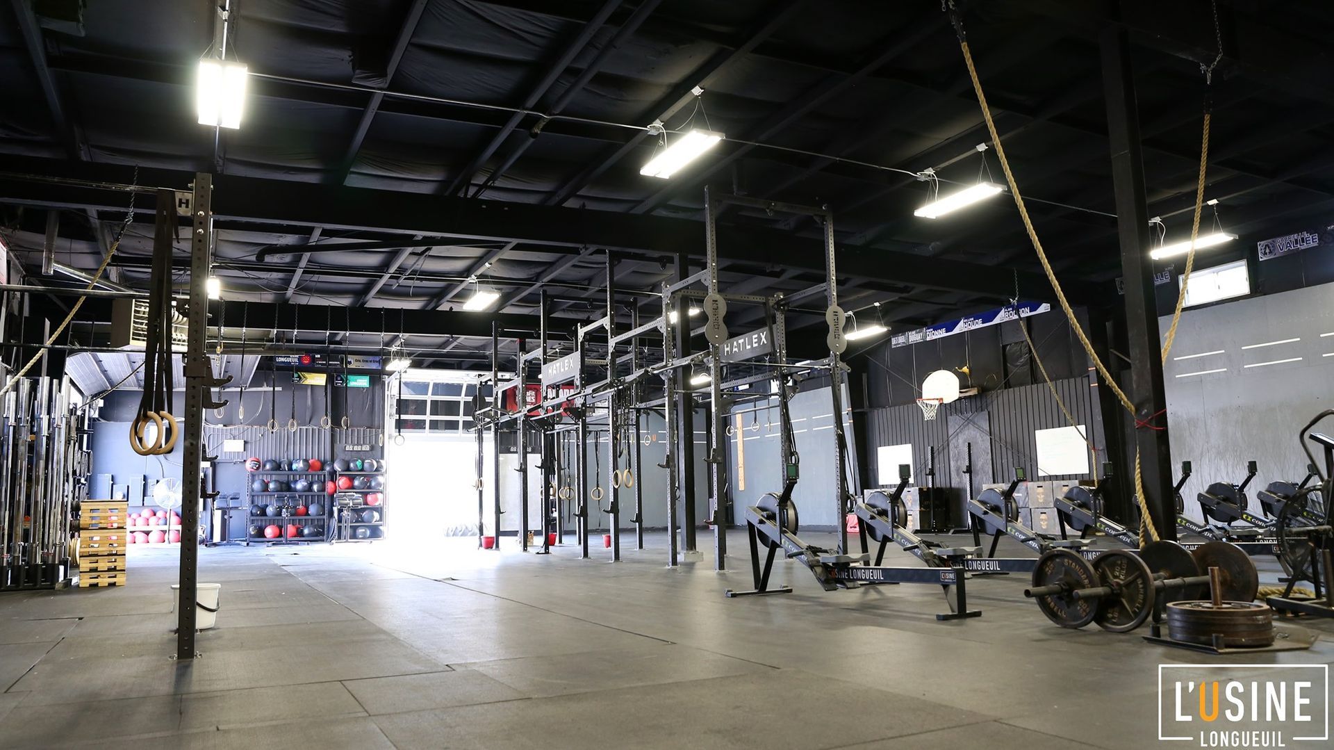 Empty gym interior with pull-up rigs, hanging straps, and workout equipment under industrial lighting