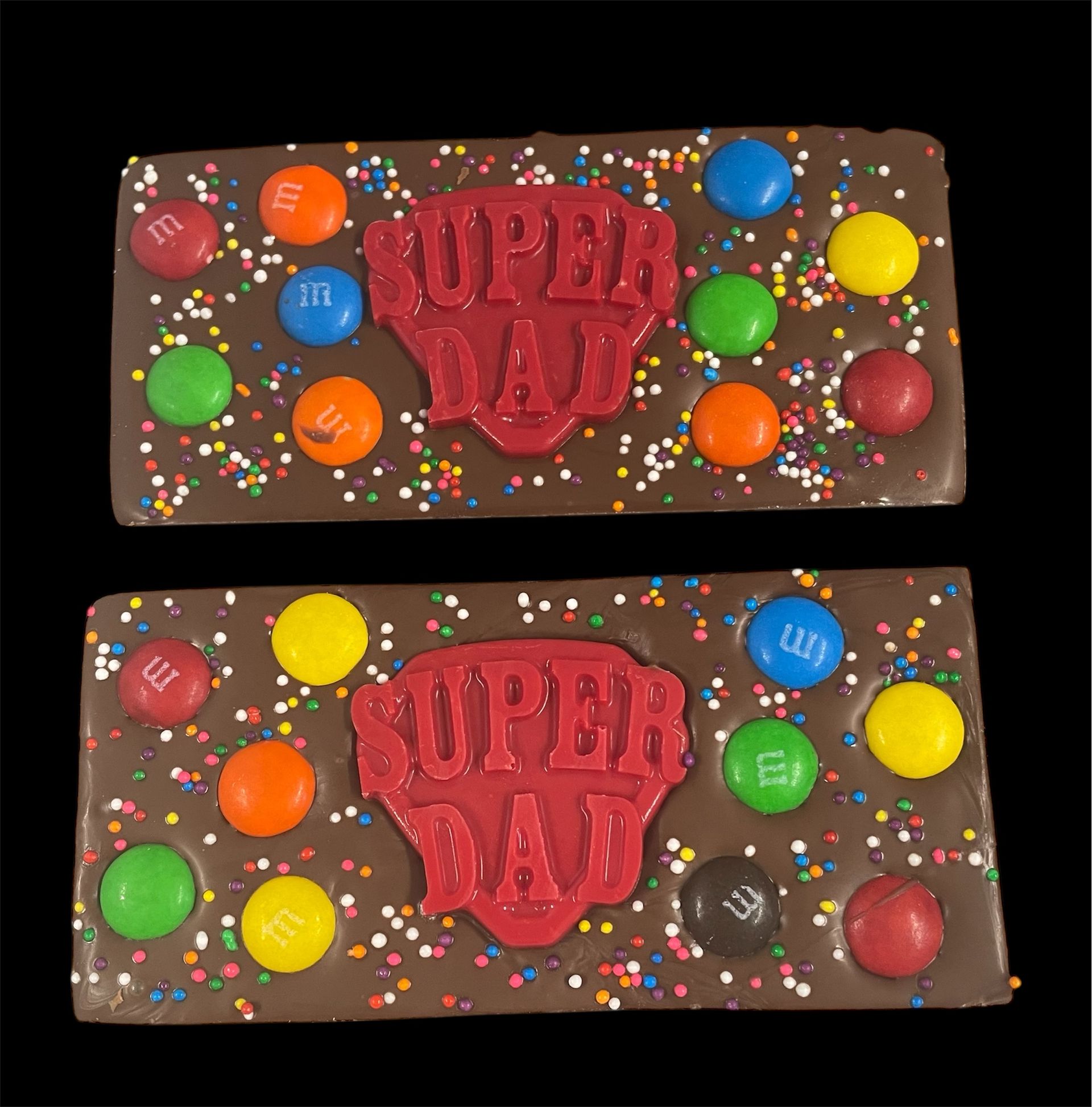 Two chocolate “Super Dad” cakes with colorful candy sprinkles and M&M’s decorations.