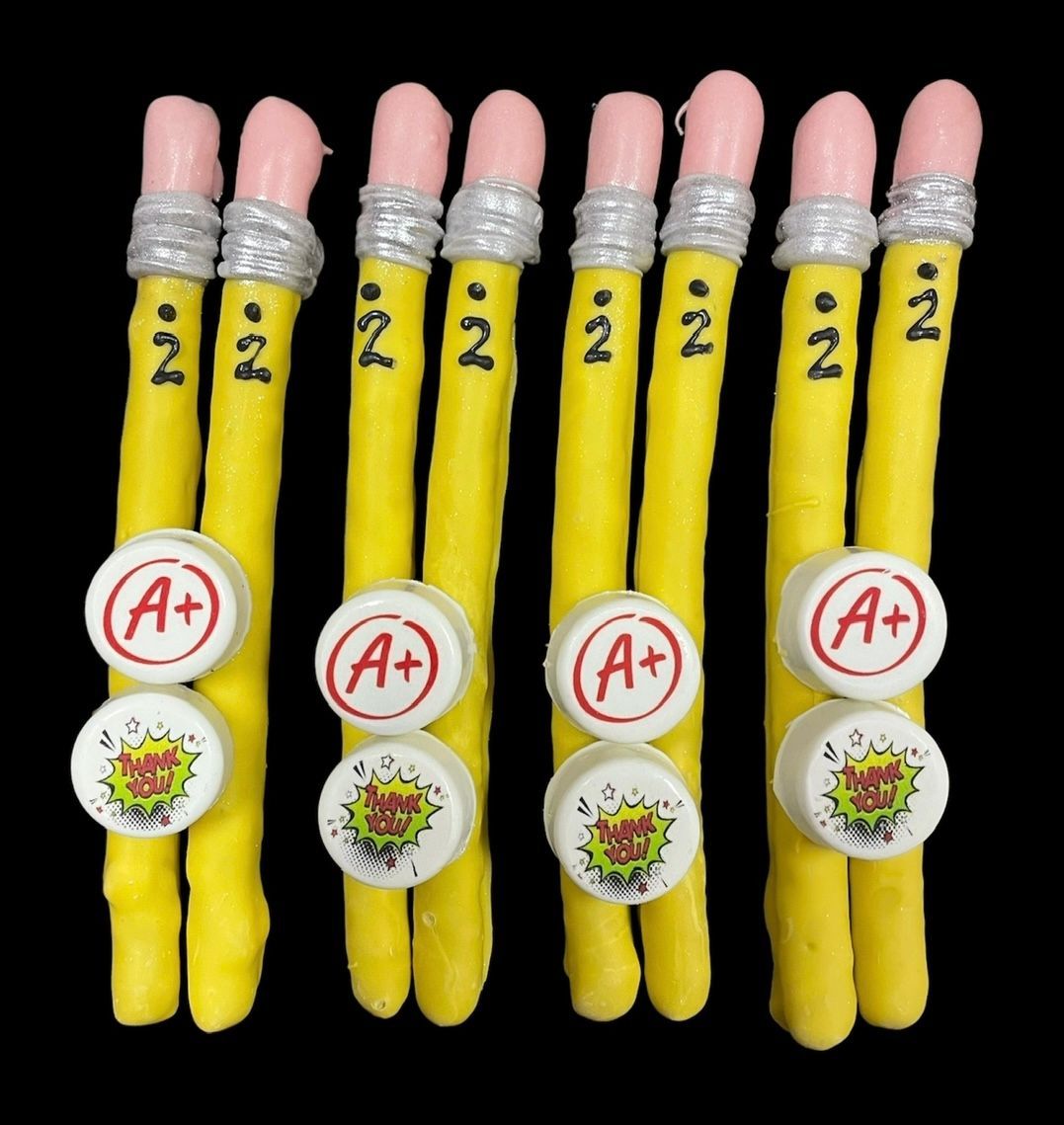 Six yellow pencils with pink erasers and A+ stickers on a black background