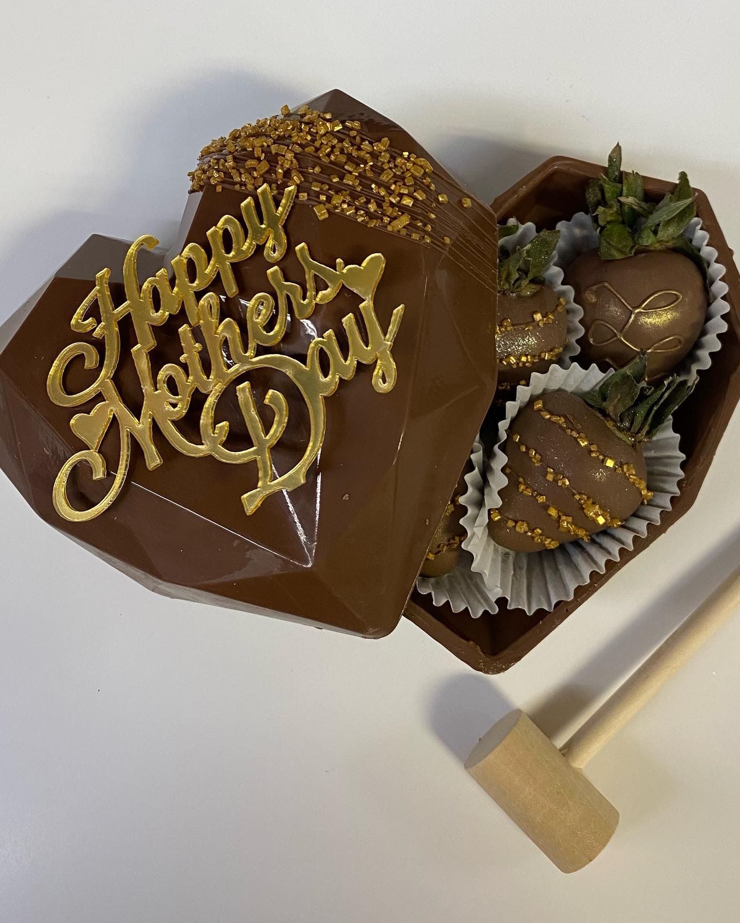 Heart-shaped chocolate box with “Happy Mother’s Day” in gold lettering and assorted chocolates inside.