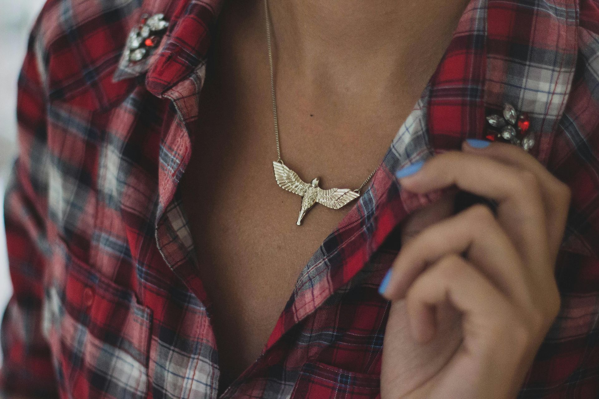 A woman wearing a plaid shirt and a necklace with a dragonfly pendant.