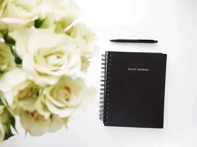 A bouquet of white roses sits next to a notebook and pen
