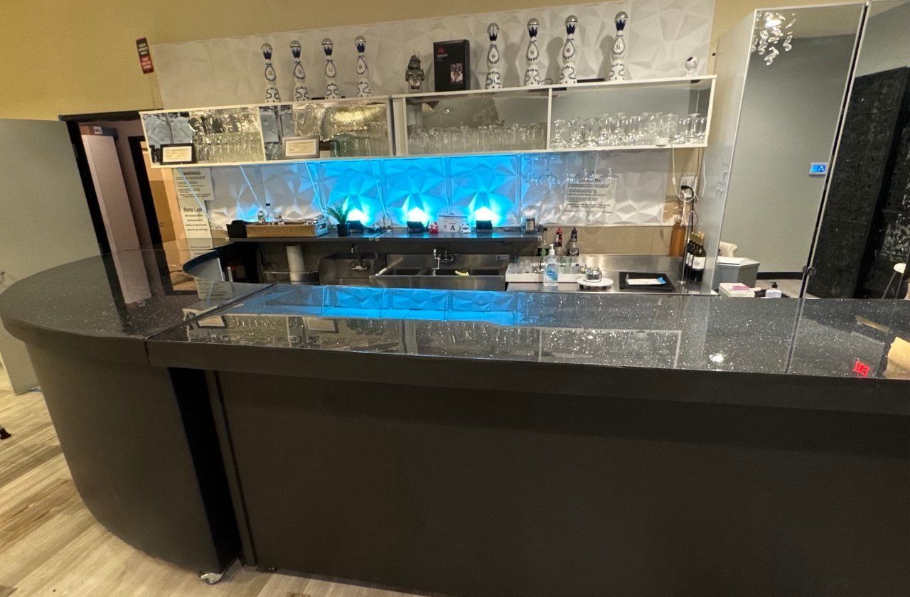 Modern hotel bar with blue backlit shelves, dark counter, and empty stools