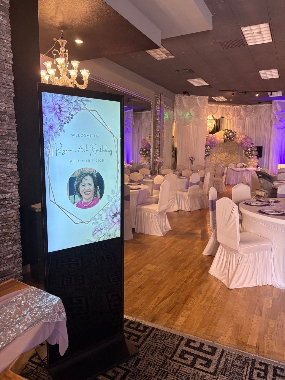 Elegant banquet hall set for an event with white table settings, tall floral centerpieces, and decorative lighting.