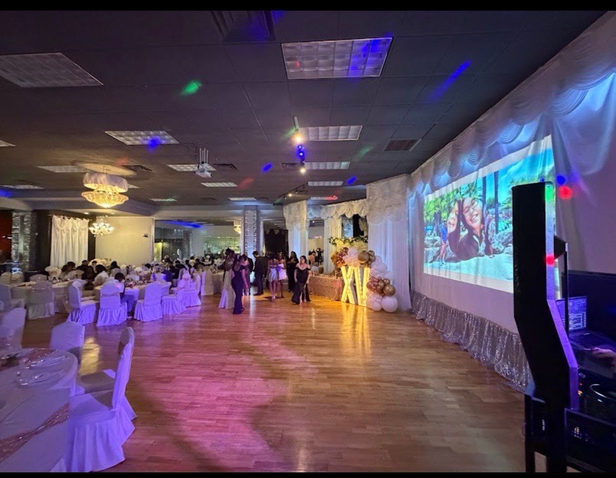 Banquet hall with seated guests, dance floor, and large colorful projected screens at an event