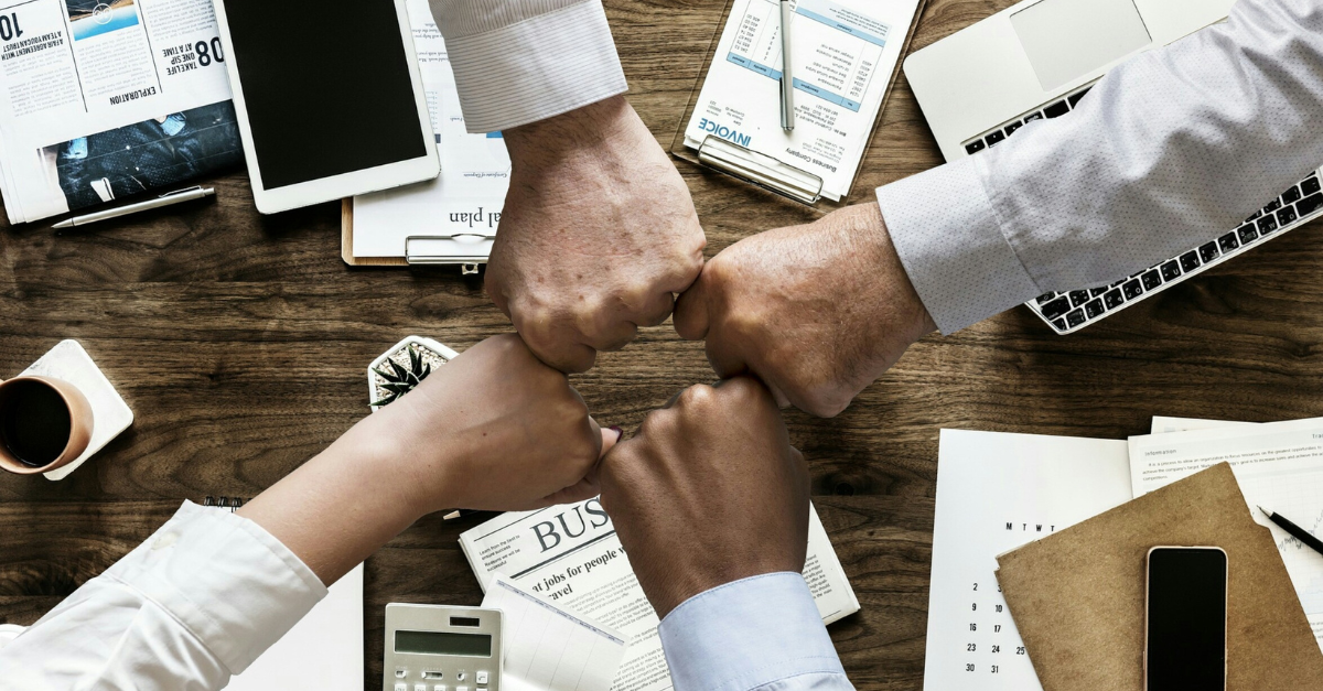 A group of people are putting their fists together on a wooden table.