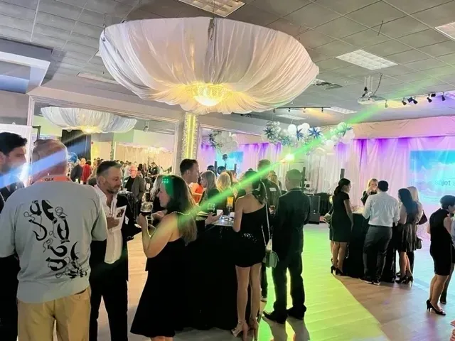 A group of people are standing in a large room at a party.