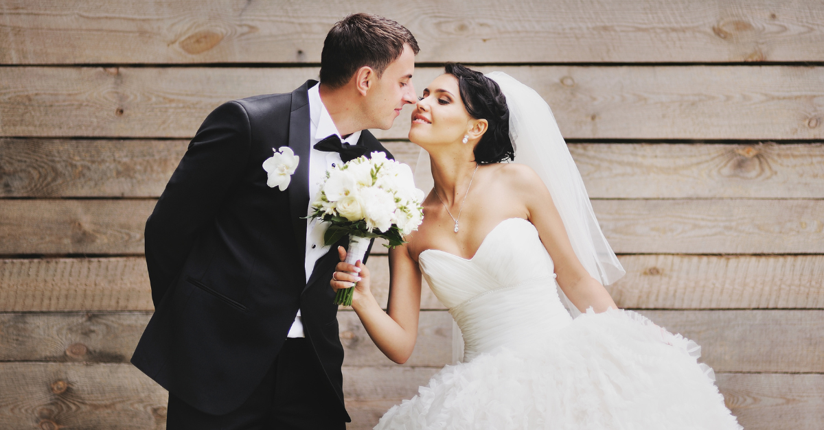 A bride and groom are kissing in front of a wooden wall.