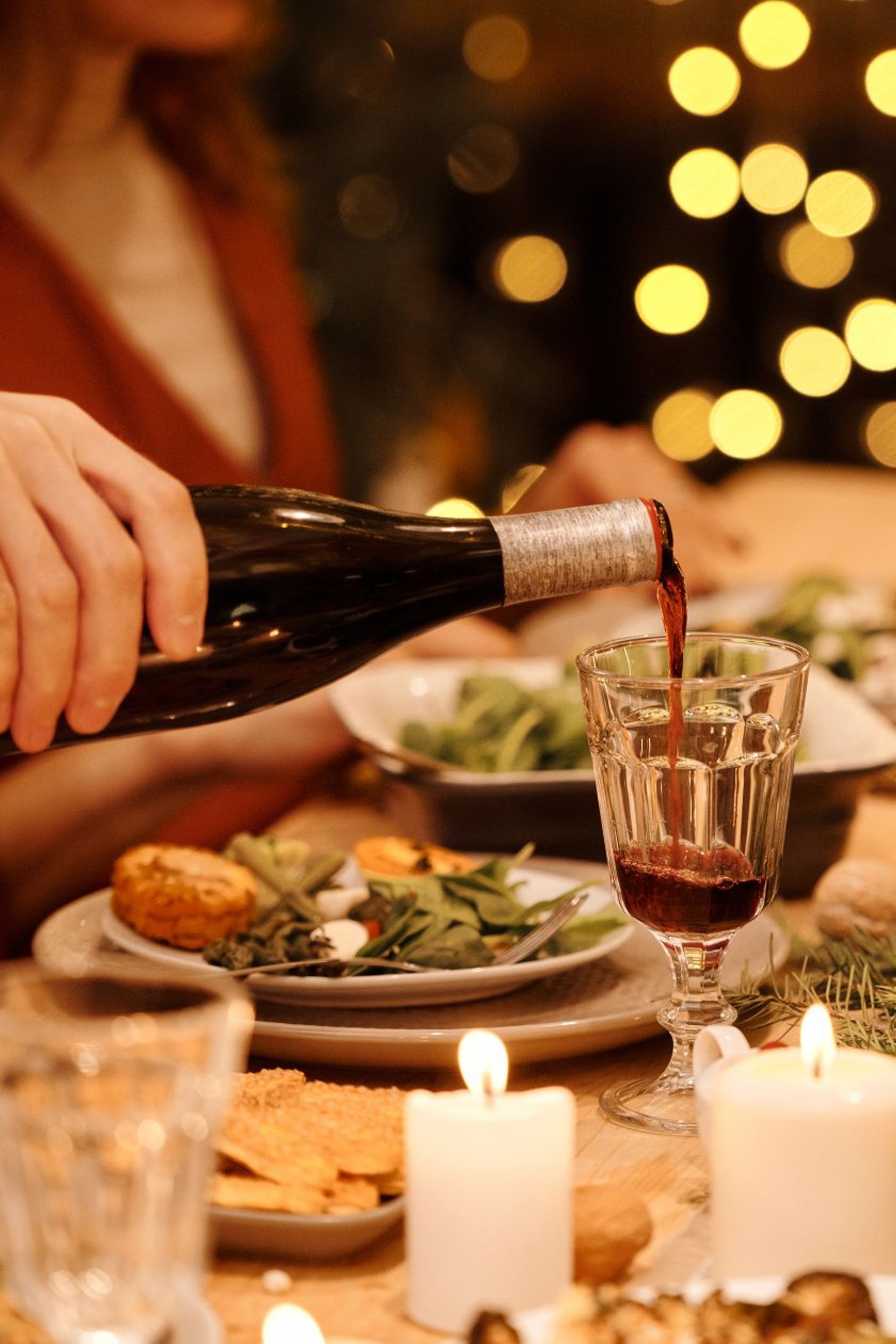 A person is pouring wine into a glass at a dinner table.