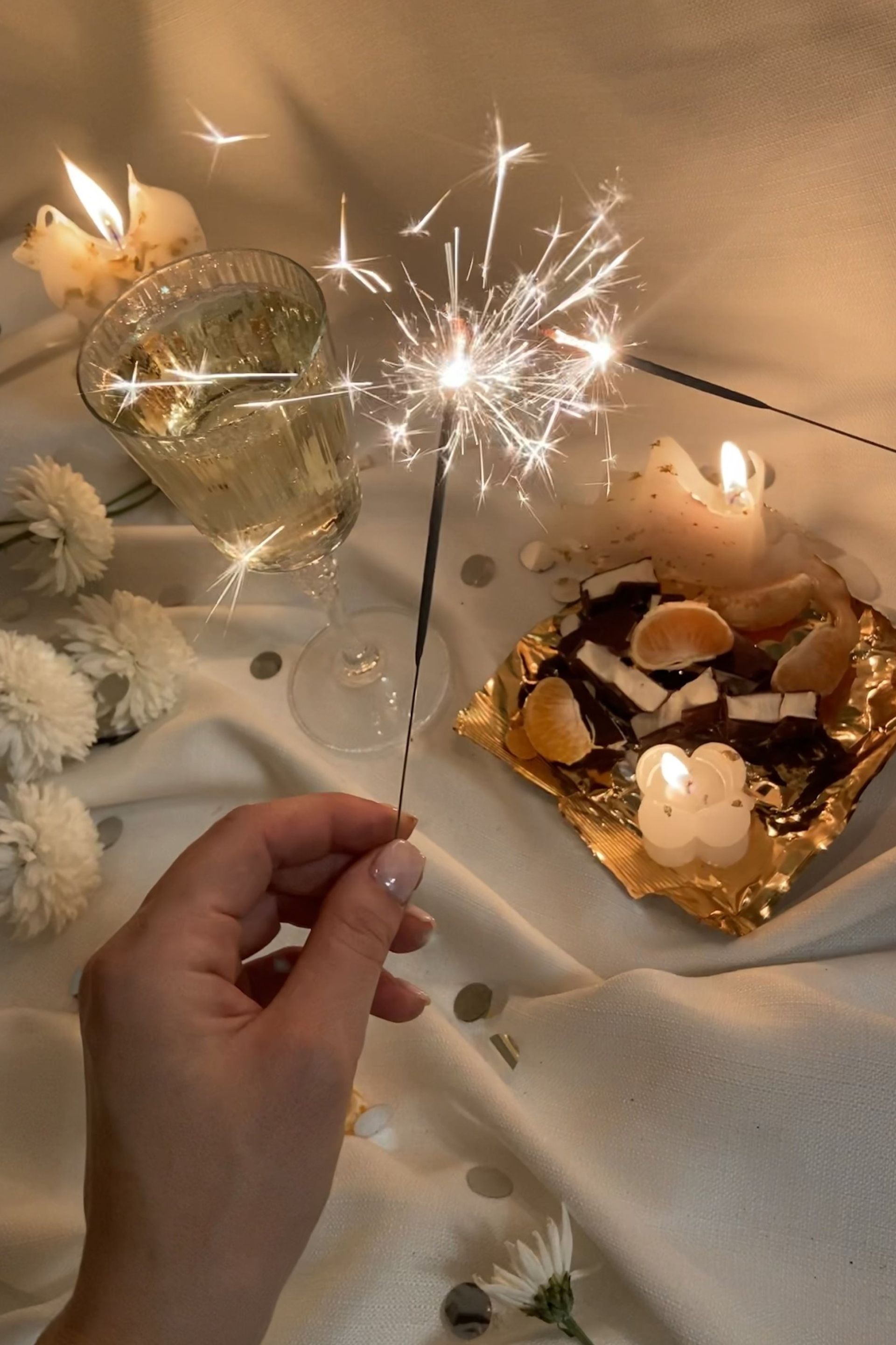 A person is holding a sparkler in front of a glass of wine.