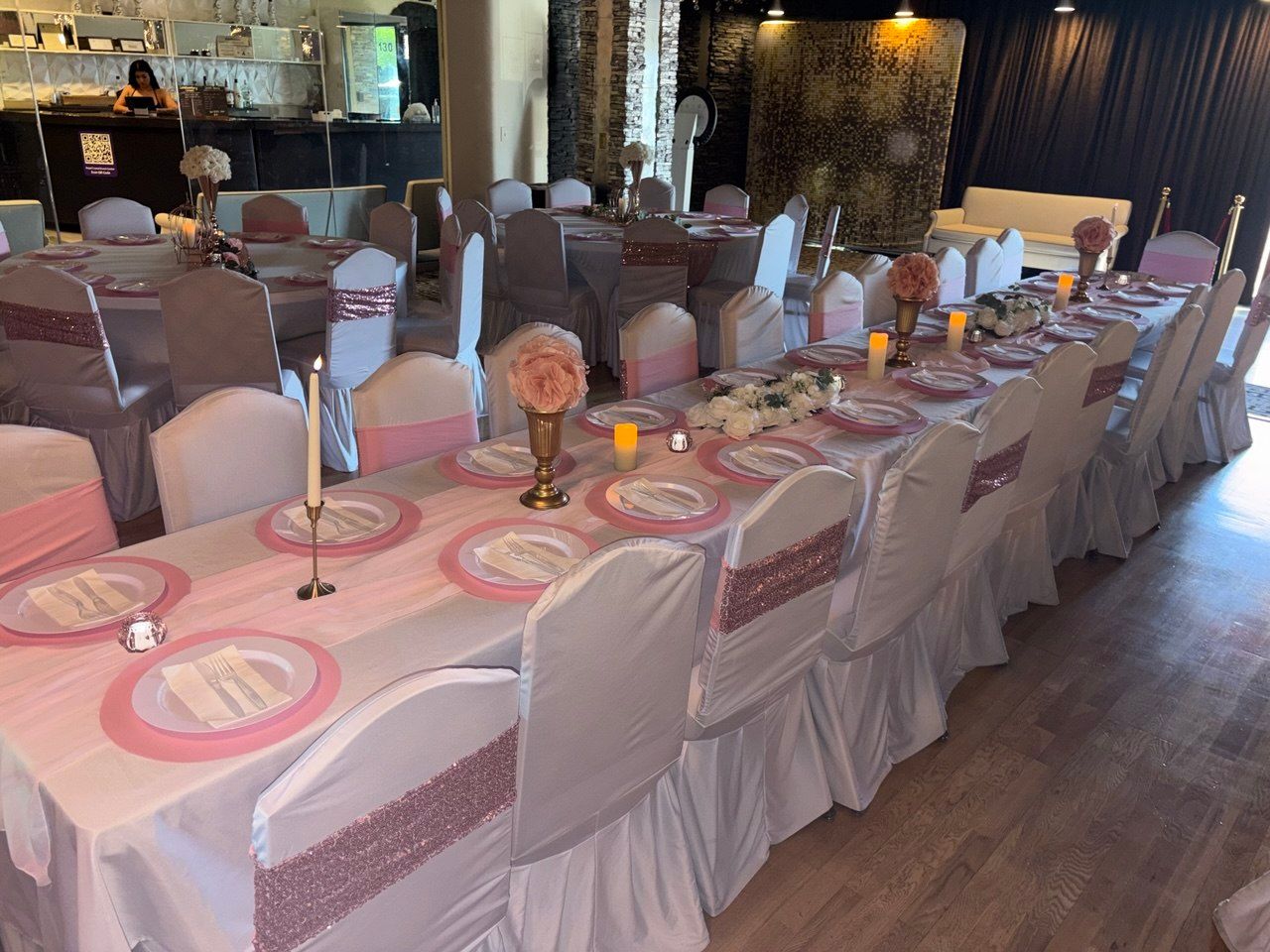 Long banquet table set with pink decor, candles, and white-covered chairs in a dimly lit event hall