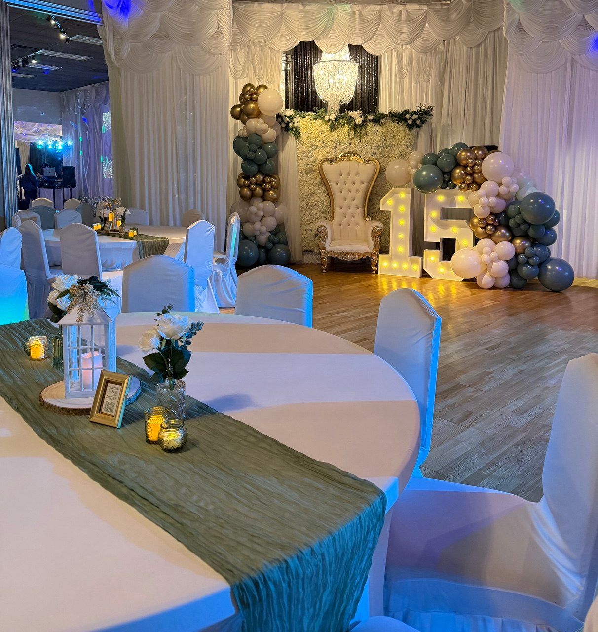 Elegant banquet hall with white and gold decor, round tables, and a lit “15” centerpiece on the stage