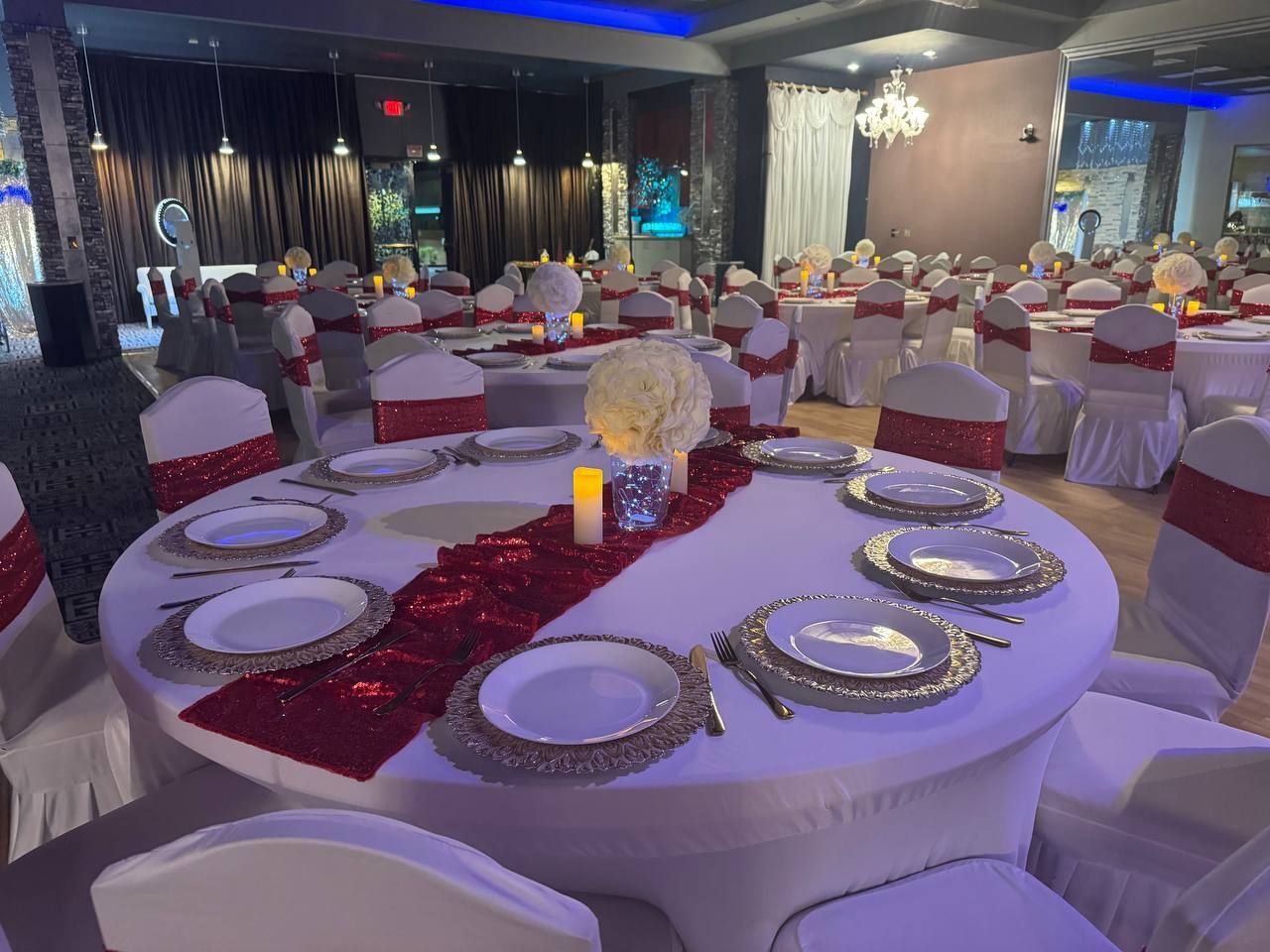 Round banquet tables set with red table runners, white chairs, and silver plates in an elegant event hall