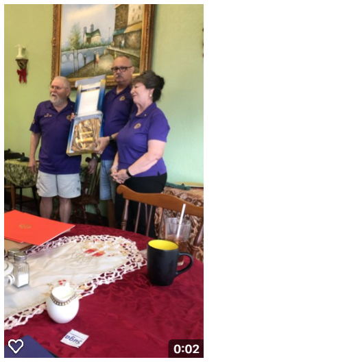 Three people in purple shirts holding an award, in a dining area with a red tablecloth.