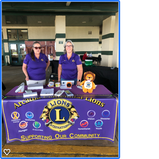 Two women at an Arcadia Lions Club booth, with purple table cloth. Supporting community.