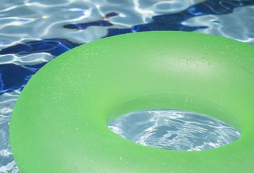 a green inflatable ring is floating in a swimming pool .