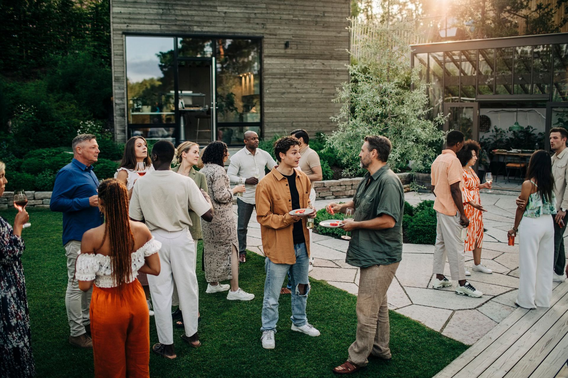People socializing at a backyard gathering; modern home, green lawn, warm sunlight.