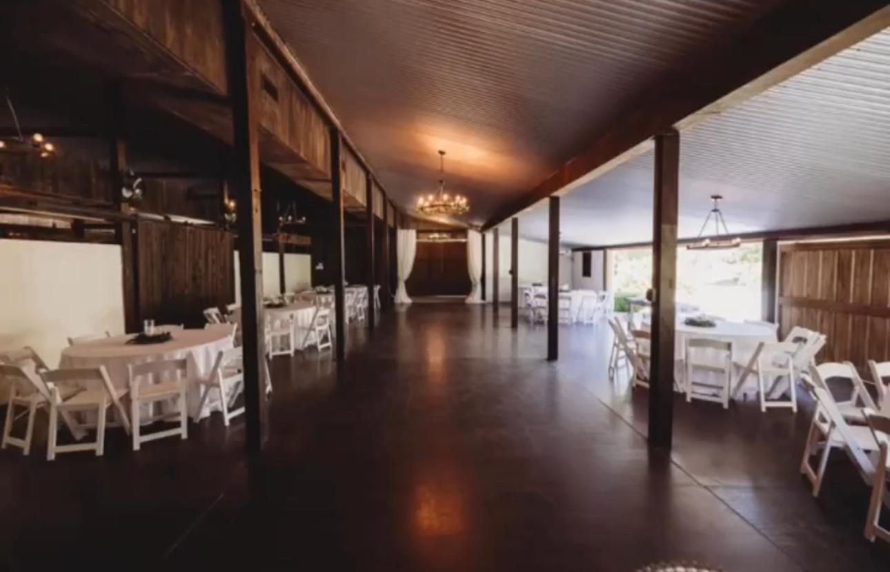 Couple kissing under floral archway during wedding ceremony. Lush greenery, rustic wooden backdrop.