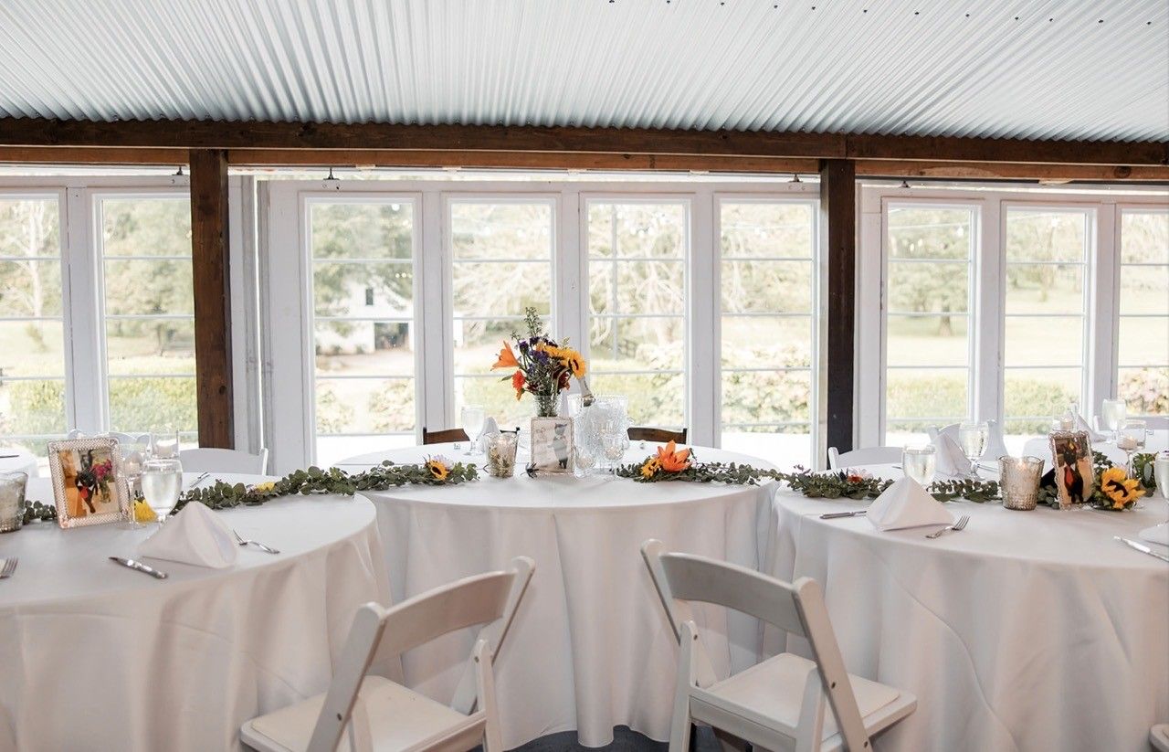Wooden table set for a celebration with white flowers, candles, and draped fabric. Outdoors.