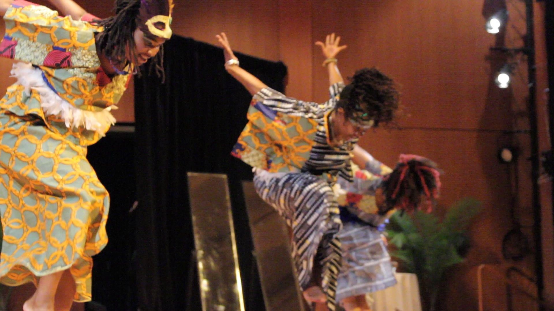 Three people dancing onstage in colorful patterned clothing.