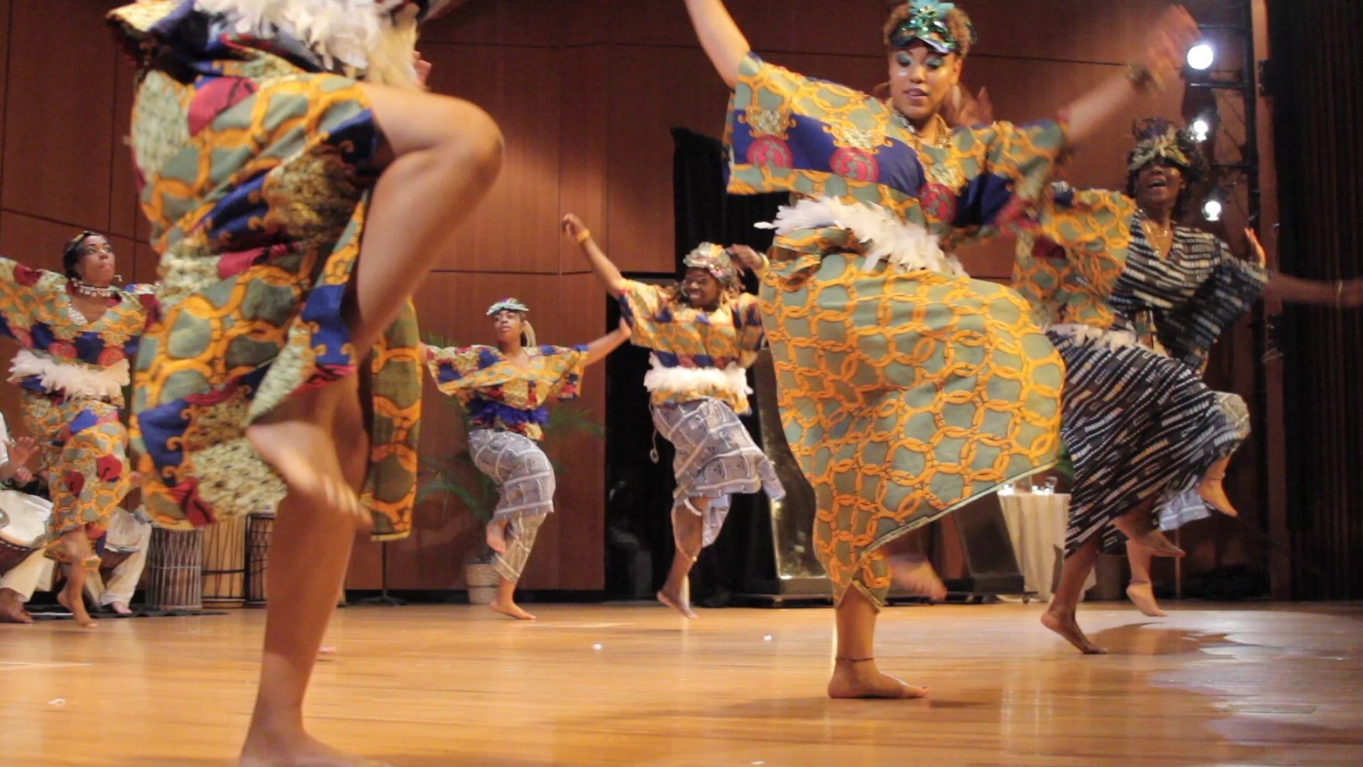 African dancers in colorful traditional attire perform on a stage.