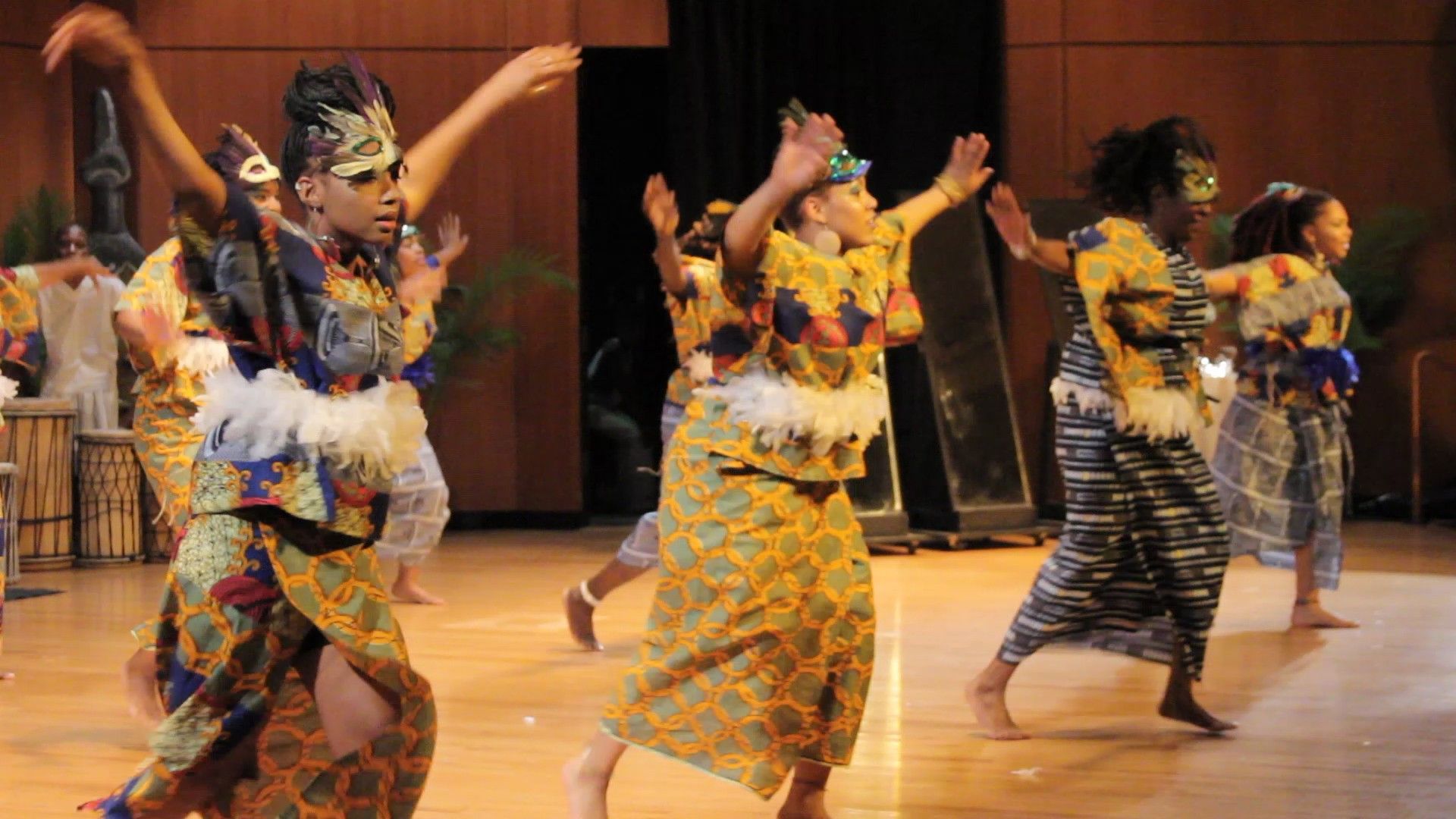 Group of dancers in colorful African attire performing on stage, arms raised.